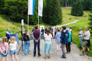 Es sind von hinten zahlreiche Personen zu erkennen, im Hintergrund wehen zwei Fahnen.